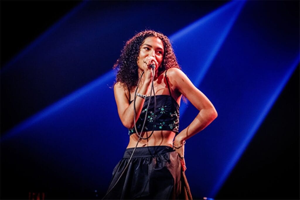 Olivia Dean sur scène, interprétant un titre en regardant le coté gauche du public 